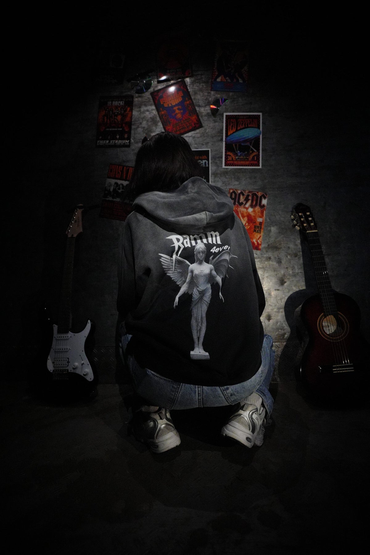 Vintage washed black streetwear hoodie with angel figure back graphic and minimalist logo design shown in a music inspired lifestyle setting.