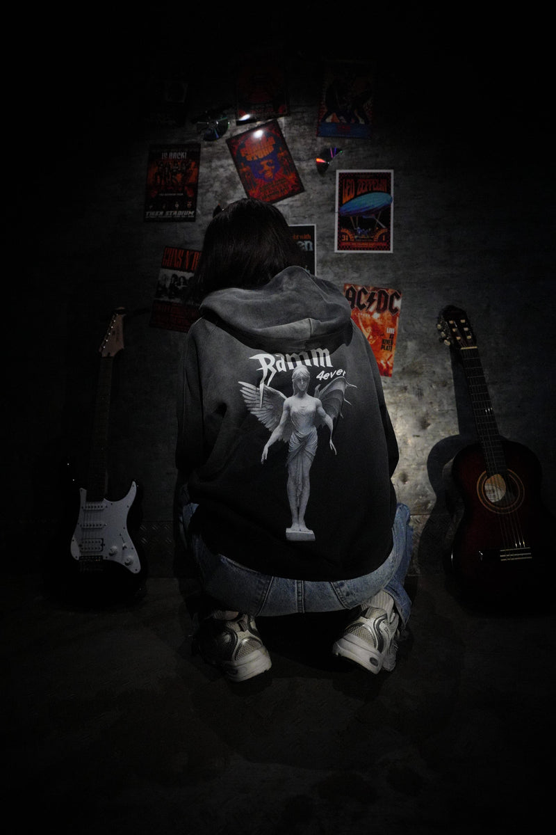Vintage washed black streetwear hoodie with angel figure back graphic and minimalist logo design shown in a music inspired lifestyle setting.