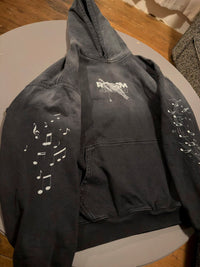 Vintage washed black streetwear hoodie with music note sleeve prints and front pocket detail shown in a top-down view.