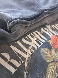 Vintage washed black streetwear hoodie with fabric texture and graphic print detail featuring raised by the 80s design in a close-up view.