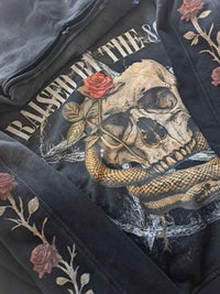 Vintage washed black streetwear hoodie with raised by the 80s graphic print detail featuring skull, snake and rose design in a close-up view.